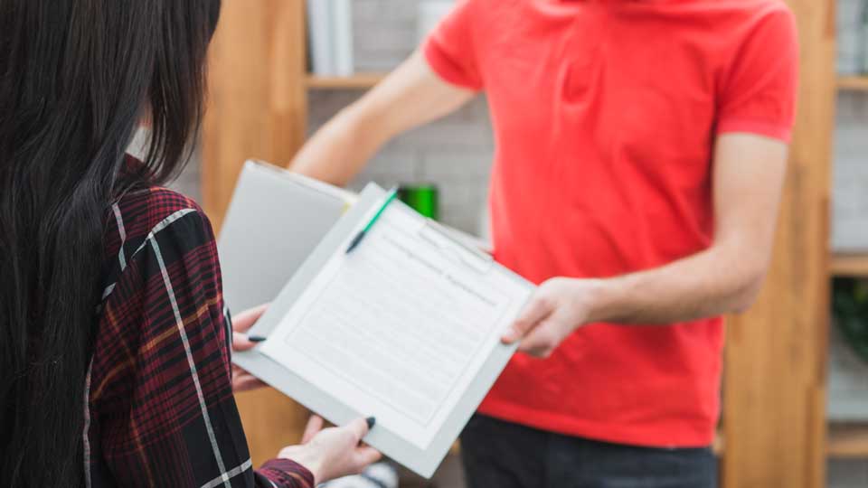 Ein Arbeiter mit Handschuhen und Schürze bearbeitet mit Werkzeugen eine schwarze Recyclingbatterie, umgeben von grünen Recyclingbehältern und umweltfreundlichen Schildern.
